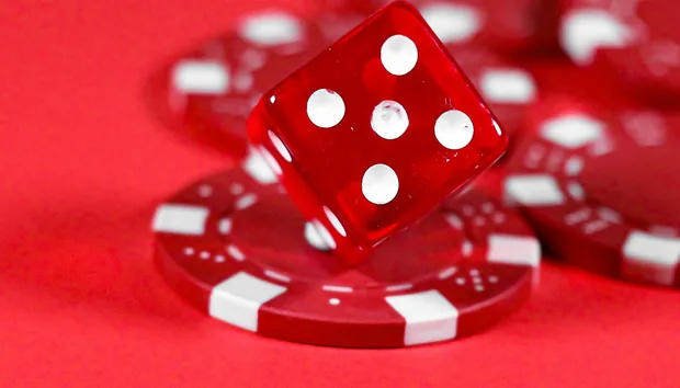 A red die tumbling onto stacks of red and white casino chips