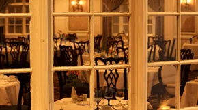 A formal restaurant dining room seen through tall glass doors